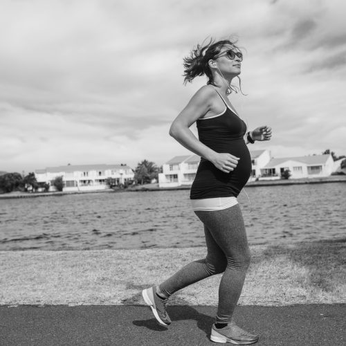 Side view of a pregnant woman on a morning walk. Woman walking near a lake listening to music.