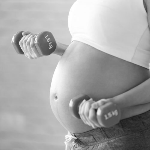 Close-up of pregnant woman doing exercise with dumbbells at home.