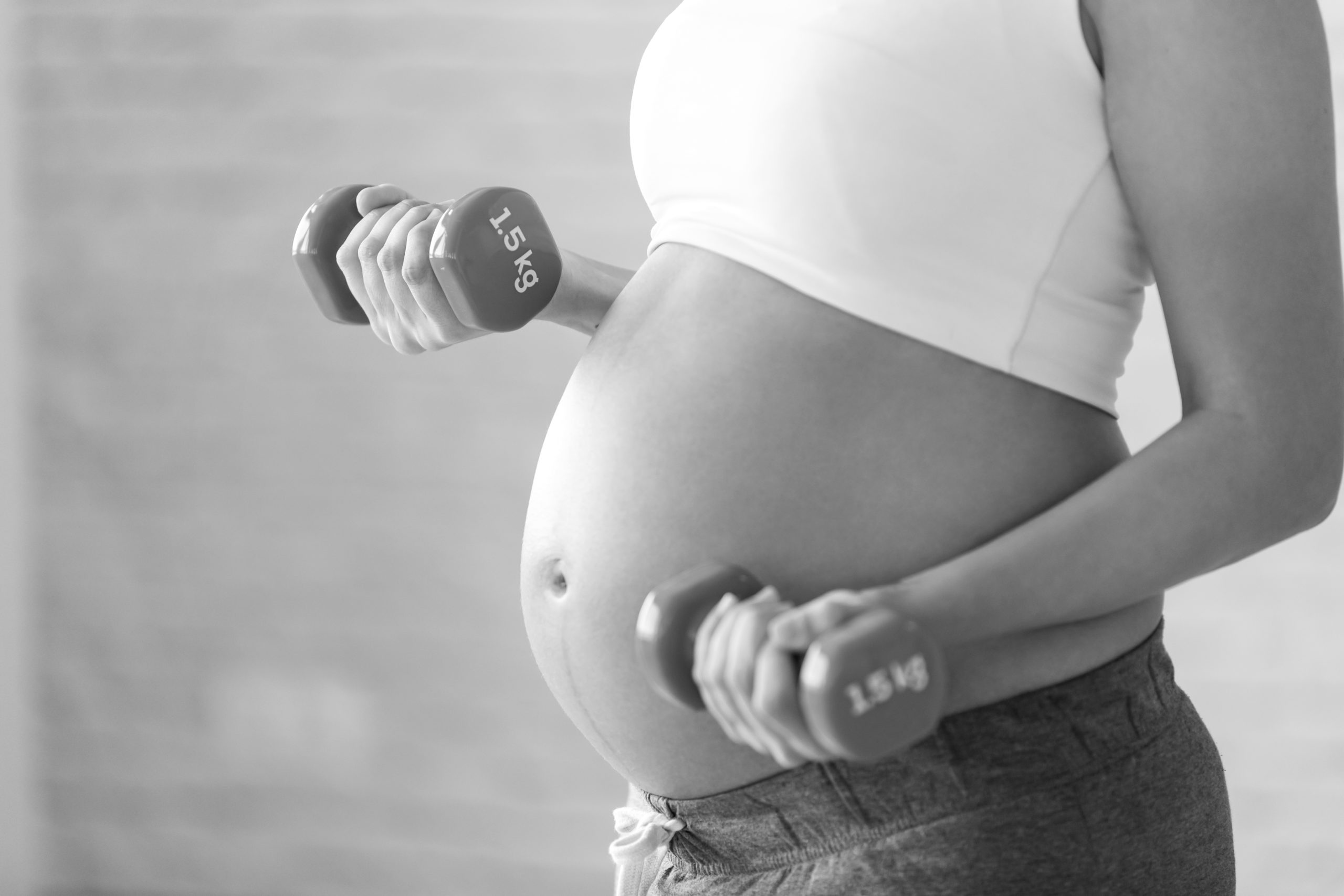 Close-up of pregnant woman doing exercise with dumbbells at home.